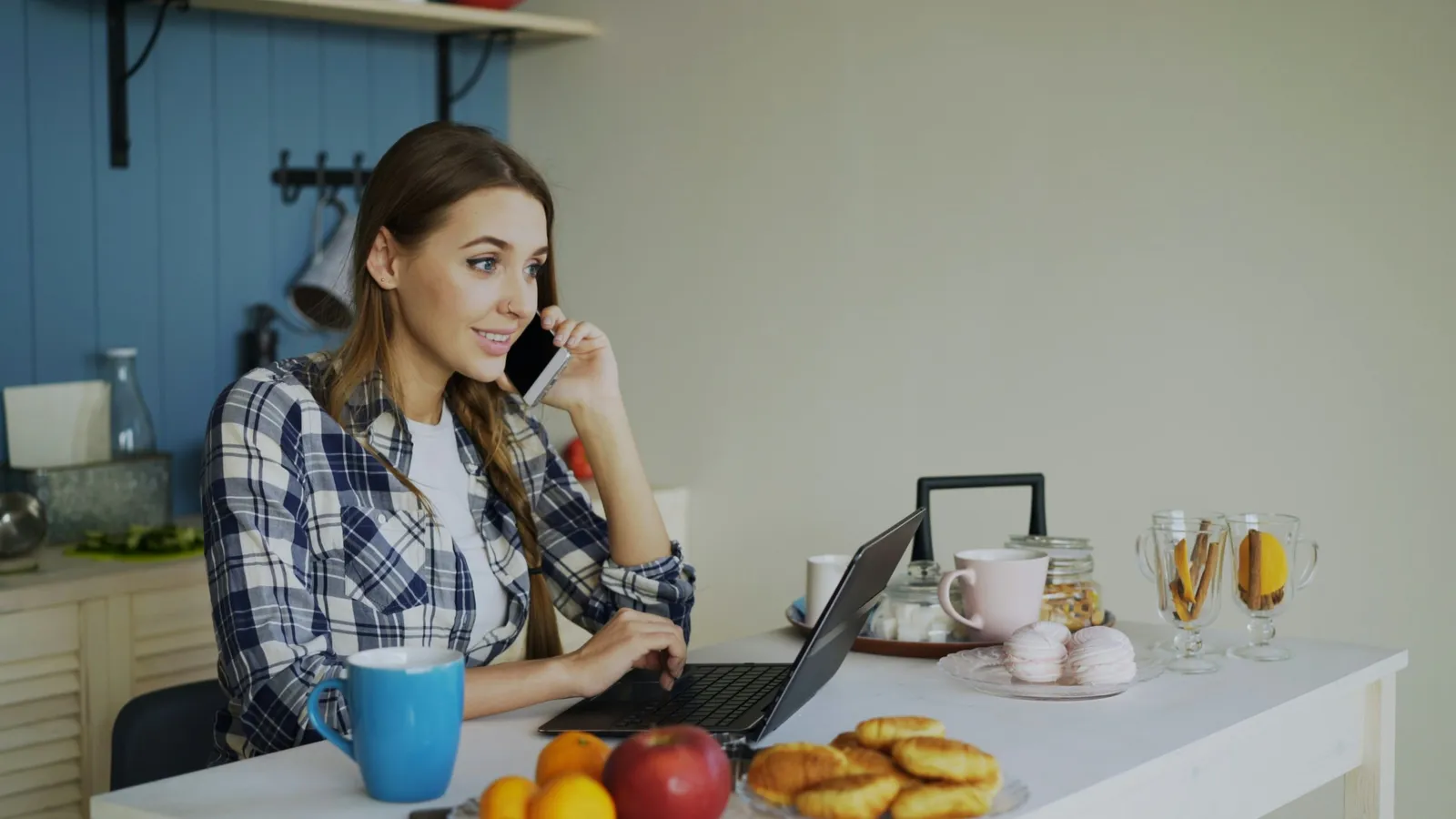 A woman at her kitchen bench on the phone with a laptop open, fitting her plan around the rest of her day
