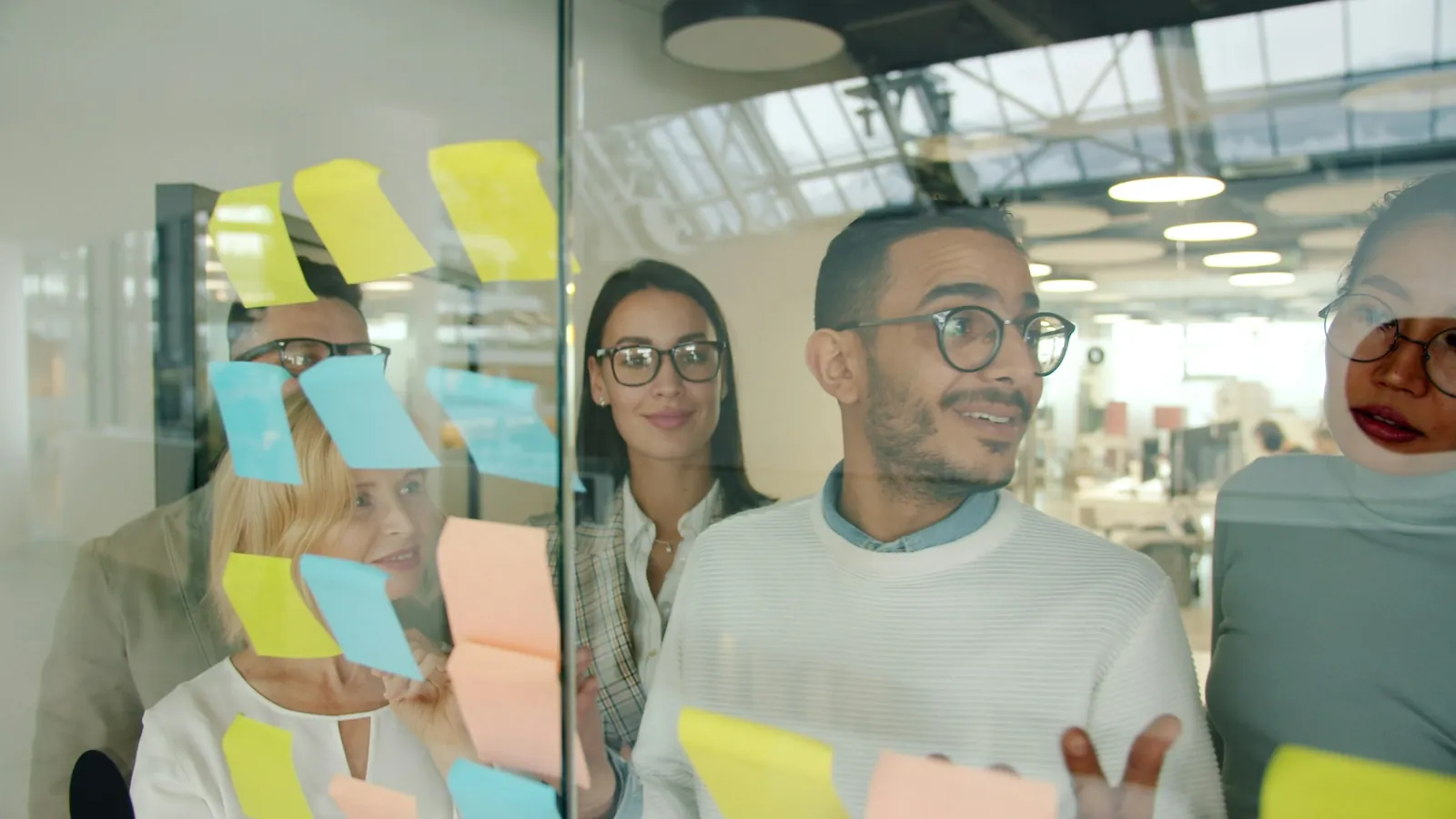 A young man discussing brand strategy with colleagues around sticky notes on a glassboard, the planning behind a growing brand