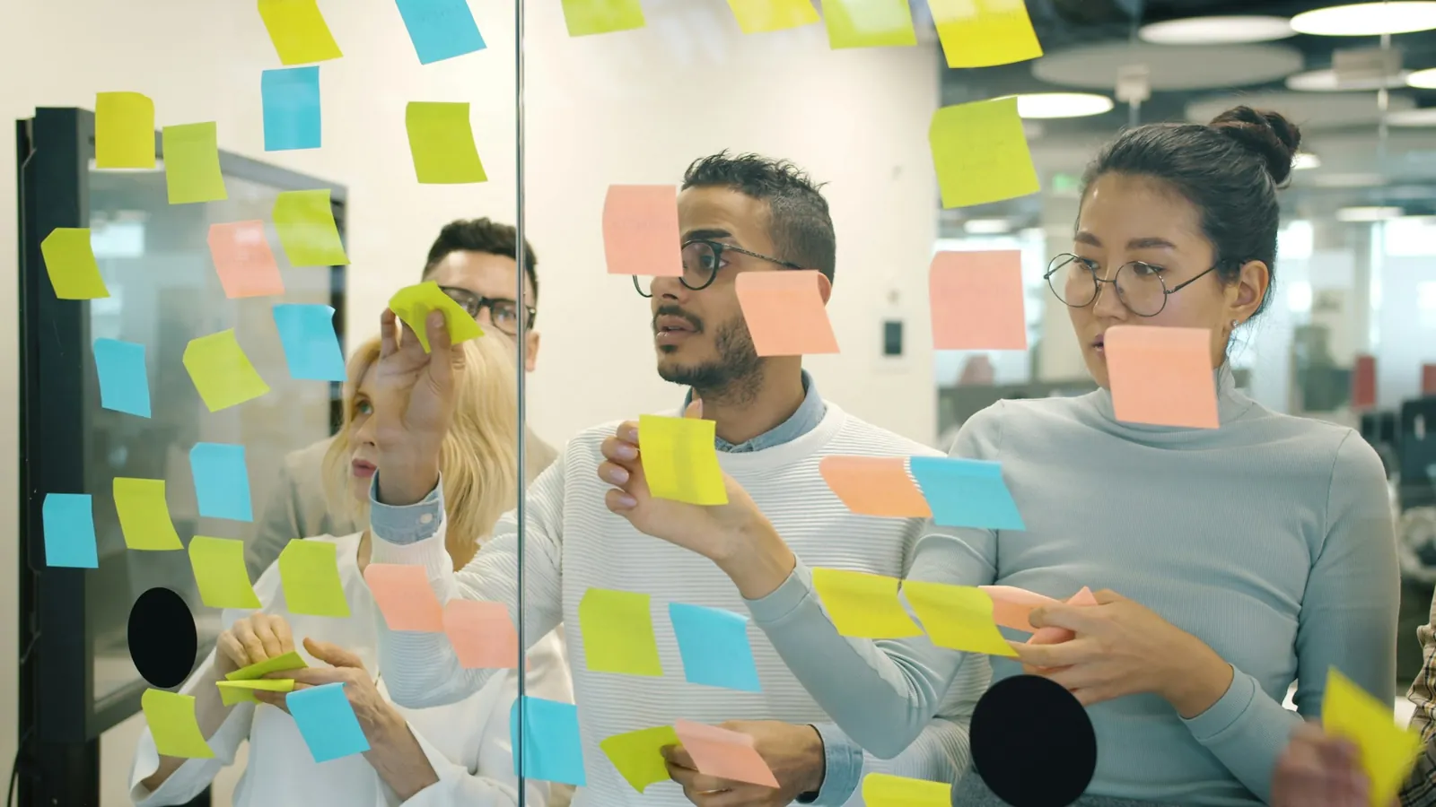 A team sticking colourful notes on a glass board in a modern office, brainstorming the strategy behind a brand