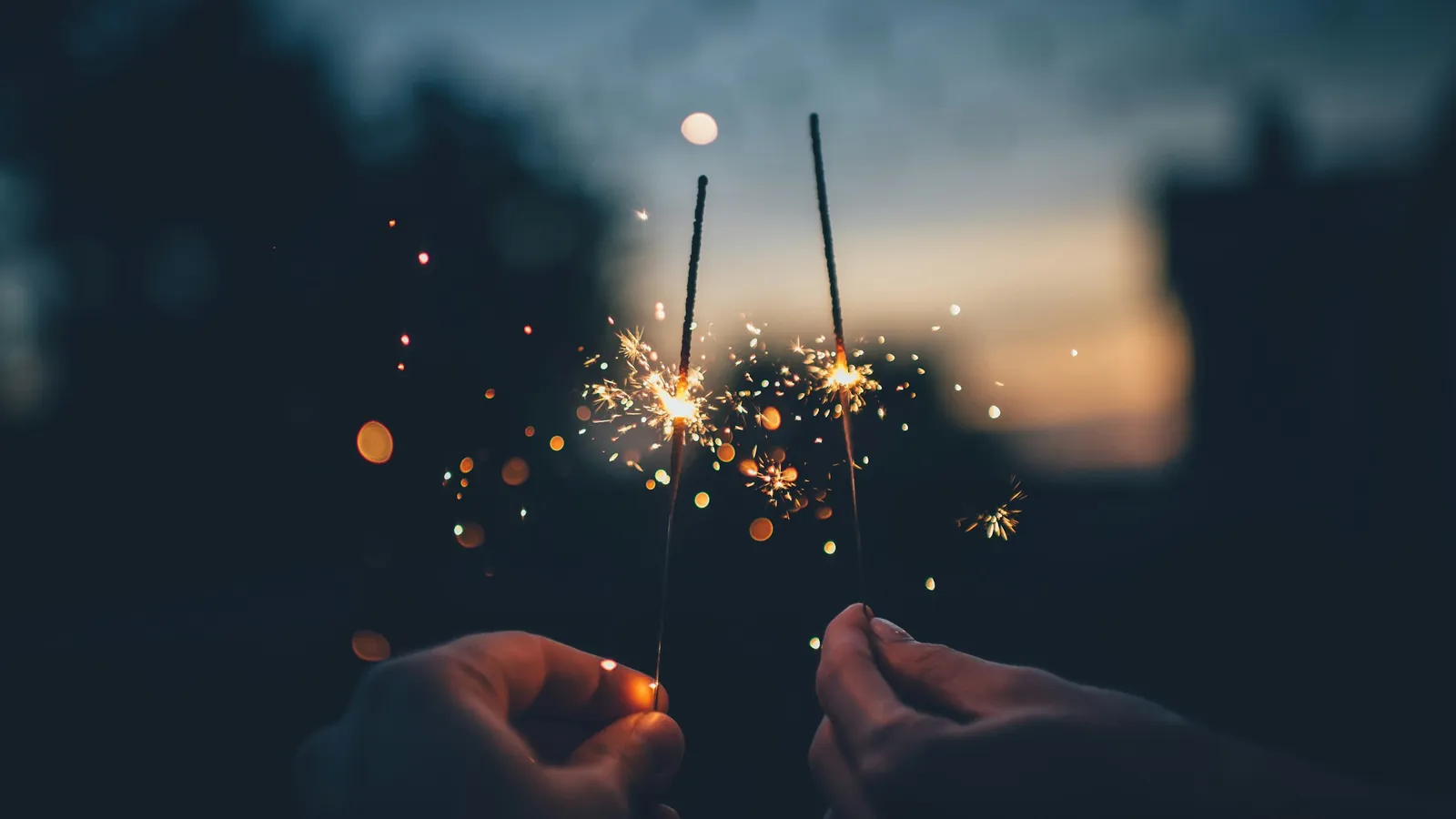Two hands holding lit sparklers at dusk, marking the start of a new year