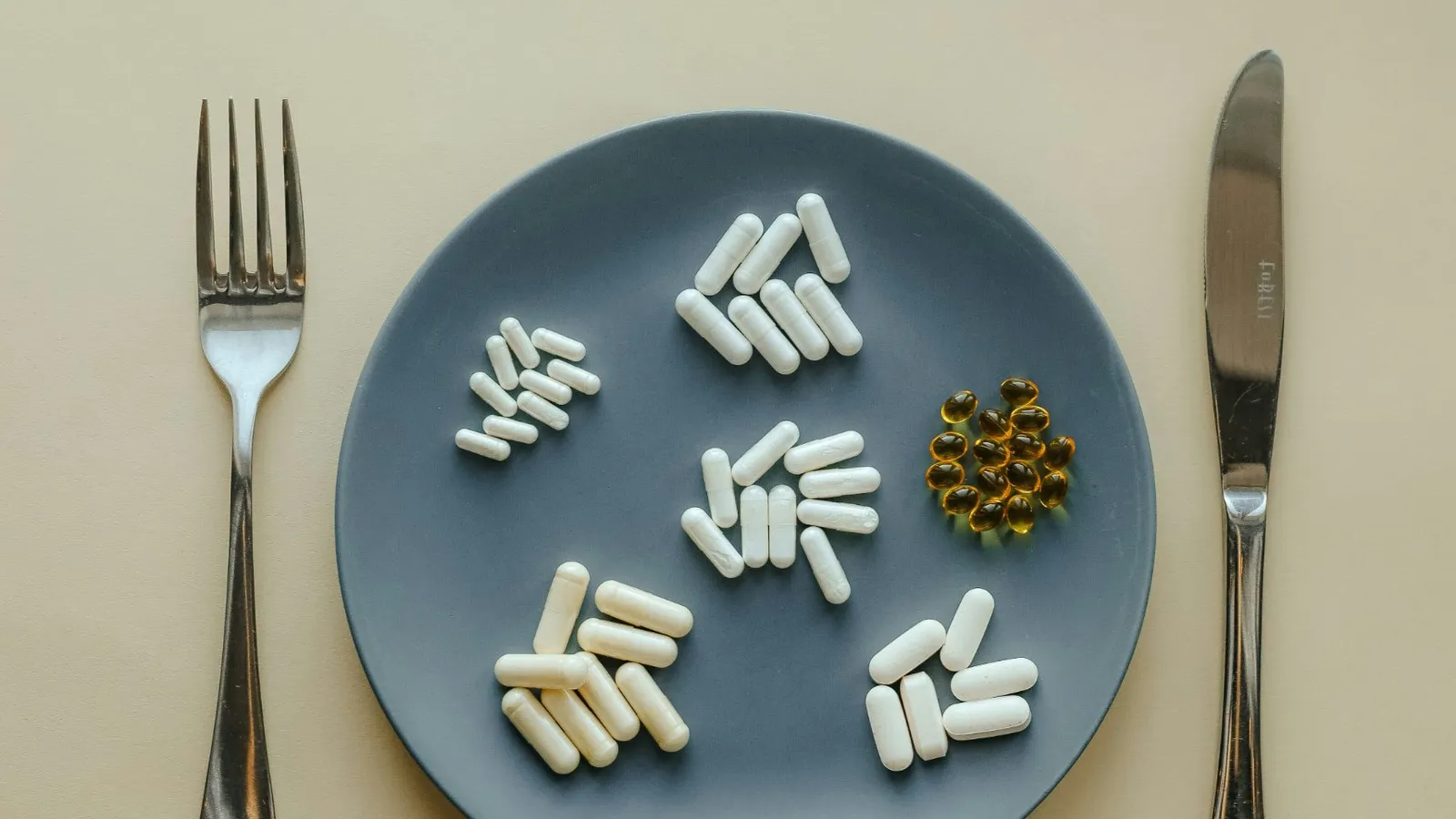 Unbranded supplement capsules grouped on a plate between a knife and fork
