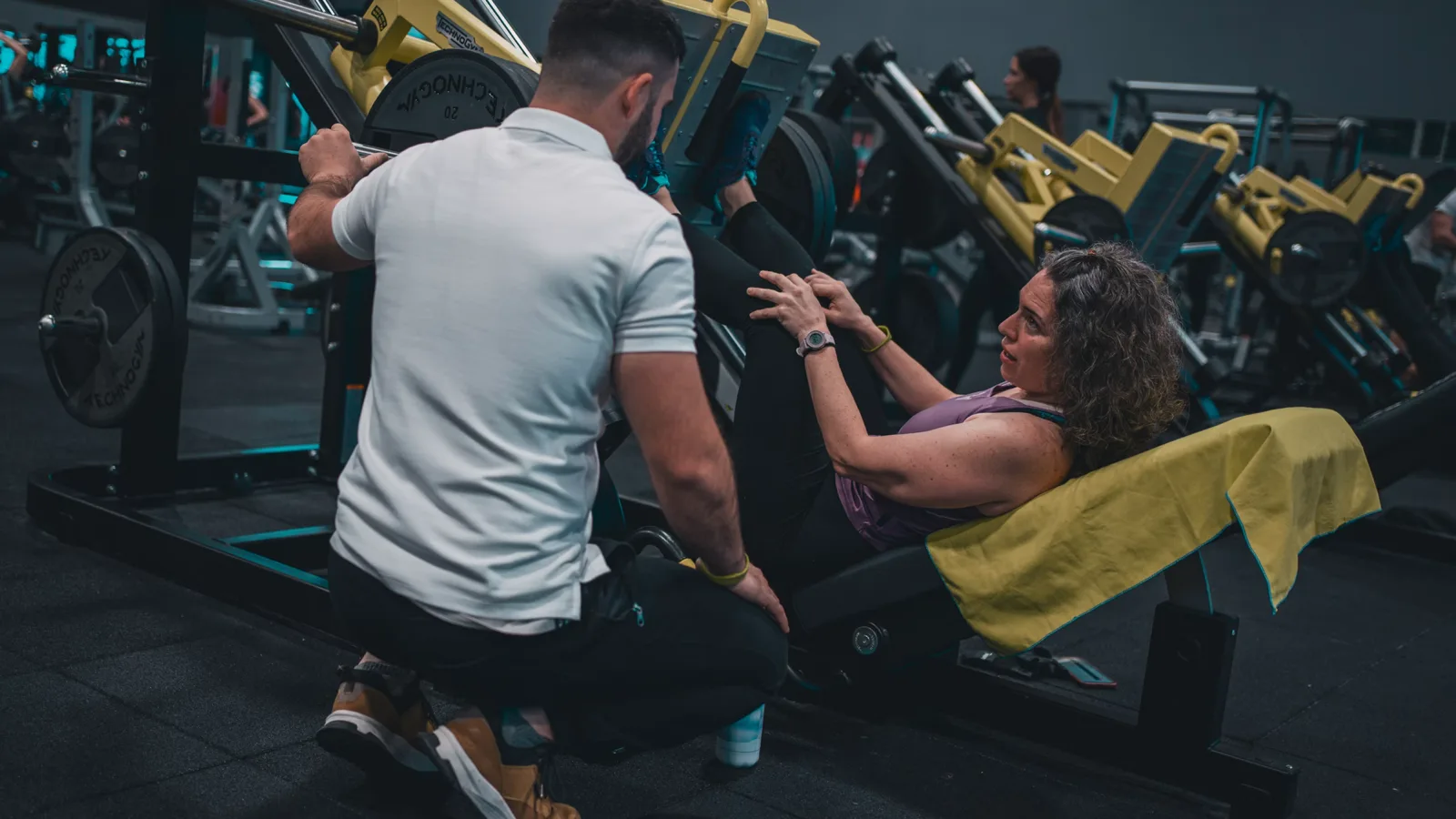 A personal trainer guiding a client through a leg press in a gym, the professional who shapes purchase decisions in health and fitness
