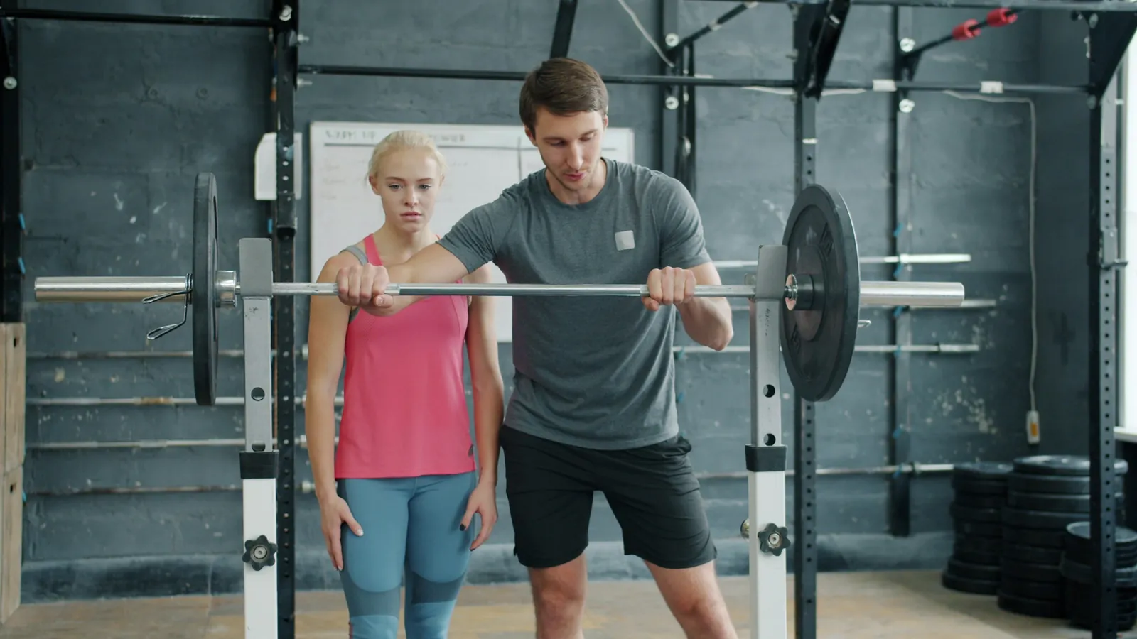 A personal trainer coaching a client through a barbell lift in a gym, the one-to-one session where a professional shapes what a client buys